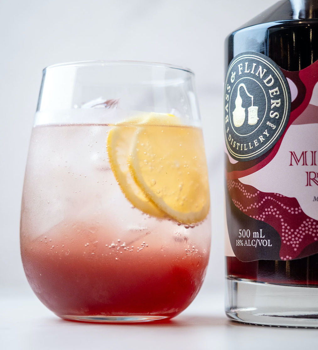 Bass & Flinders Distillery Pineau Spritz in glass garnished  with lemon slices beside bottle of Mistelle Rouge