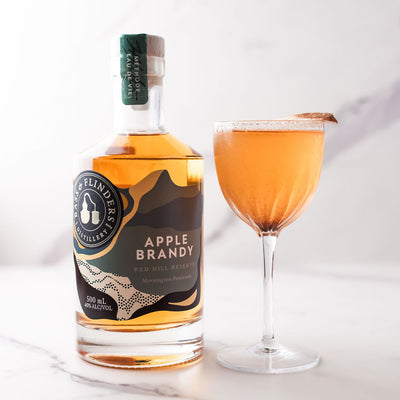 Bottle of bass & Flinders Distillery Apple Brandy with a Golden Orchard apple brandy cocktail in glass on a white background