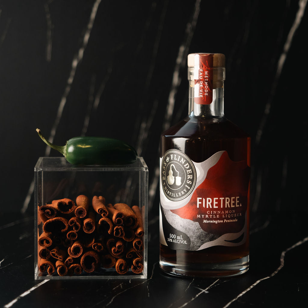 bottle of Bass Flinders Distillery Firetree Cinnamon myrtle liqueur next to hot green chilli and cinnamon botanicals