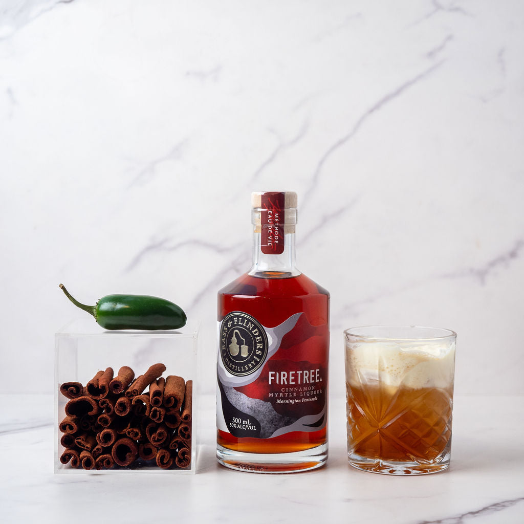 Bass Flinders Distillery Firetree Cinnamon myrtle liqueur in bottle with Spiced Russian cocktail in glass next to cinnamon and chilli botanicals 