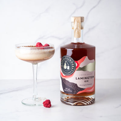 Bottle of bass & Flinders distillery Lamington Gin with a cocktail and raspberries on a white background