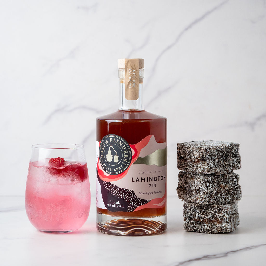 Bottle of Bass & Flinders Lamington Gin with a spritz cocktail in glass and lamingtons on a marble surface