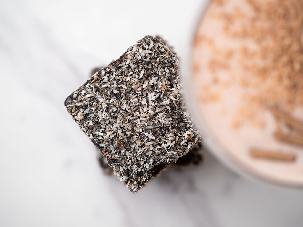Square of lamington cake with a lamington gin cocktail in the background on a white surface