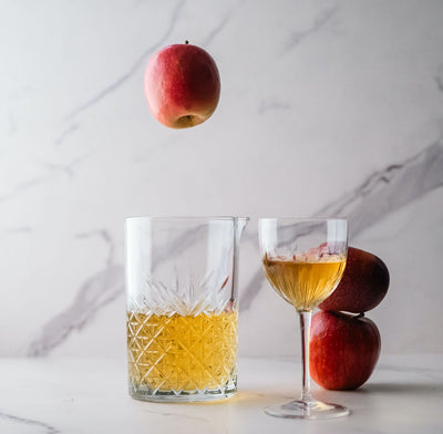 Two glasses of bass & flinders distillery apple brandy with falling apple and 2 stacked apples on a marble surface