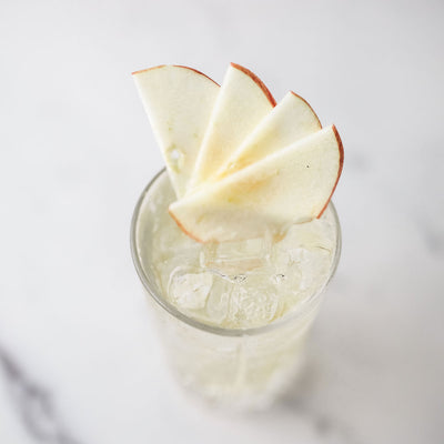 Bass & Flinders Distillery apple brandy spritz in a tall Glass topped with dry ginger ale and apple slices on a light background