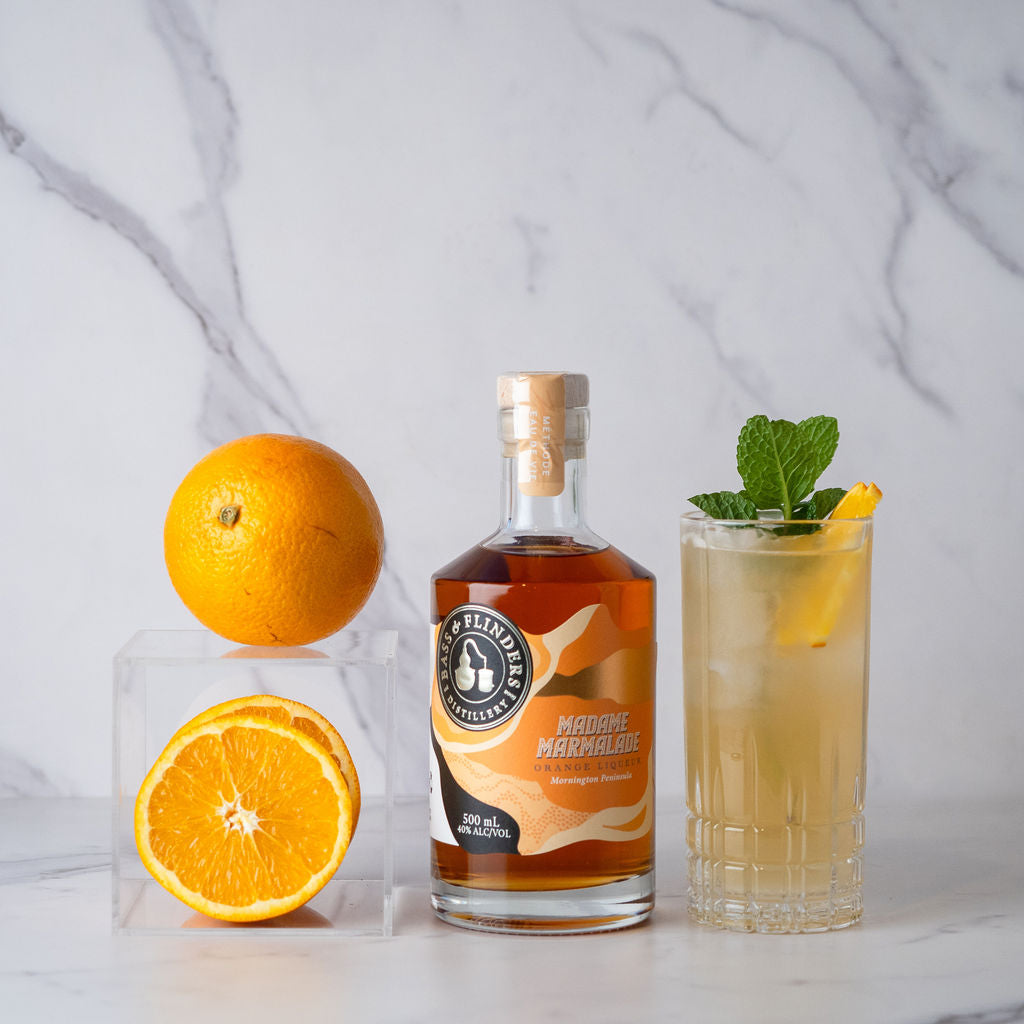 Bottle of bass & flinders distillery Madame Marmalade liqueur with oranges and a madams mule cocktail on a marble surface