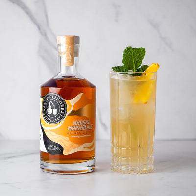 Bottle of Bass & Flinders Distillery Madame Marmalade Orange Liqueur with a Madams Mule cocktail garnished with a lemon and mint leaf on a white background.