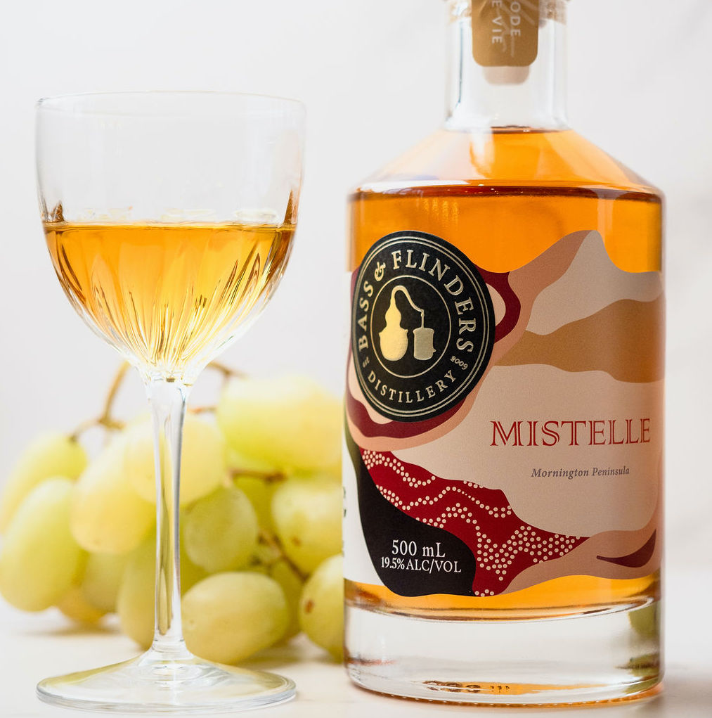 Bottle and glass of Bass & Flinders Mistelle spirit with bunch of white grapes in the background